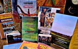 Książki regionalne wyłożone na stoliku, a za nimi obraz z tłem starej chaty kociewskiej