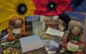 Książki regionalne wyłożone na stoliku z widocznymi tytułami obok laki kociewskie, a za nimi położone sztuczne korony kwiat&oacute;w w kolorze niebieskim, czerwonym i ż&oacute;łtym