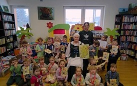 Zdjęcie grupowe dzieci z Panią Krystyną, kt&oacute;ra trzyma mapę kociewską, obok stoi bibliotekarka z Pinczyna. Dzieci trzymają kolorowanki kociewskie.