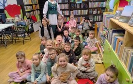 Dzieci siedzą na dywanie, a za nimi stoi Pani Krysia Kamińska w stroju kociewskim