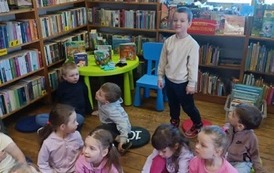 Dzieci siedzą na siedziskach w bibliotece w Borzechowie i słuchają bajki