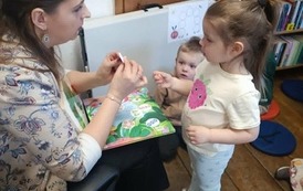 Mała dziewczynka stoi przy bibliotekarce i dostaje naklejkę z jedzeniem dla gąsienicy.