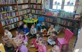 Dzieci siedzą na siedziskach w bibliotece w Borzechowie i słuchają bajki