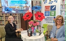 Pisarka przy stoliku podpisuje na książce dedykację czytelniczce, kt&oacute;ra siedzi obok. Obie się uśmiechają.
