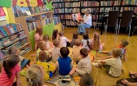 Dzieci siedzą na dywanie i patrzą na Panią Jolę, ktora im czyta bajkę obrazkami skierowaną do dzieci