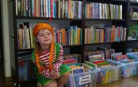 Dziewczynka przebrana za Pippi Langstrump siedzi przy regałach z książkami w bibliotece w Pinczynie