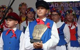 Stoją dzieci w strojach kociewskich, chłopiec z przodu trzyma statuetkę Ambasador Kociewia.
