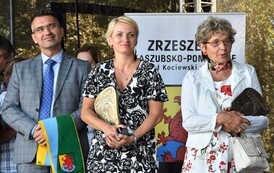 Stoją: mężczyzna i dwie kobiety, kobiety trzymają statuetki Ambasador kociewia, a mężczyzna trzyma szalik z gryfem kociewskim.