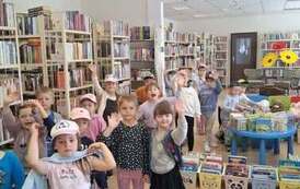 Dzieci stoją szykując się do wyjścia z biblioteki, niekt&oacute;re machają ręką.
