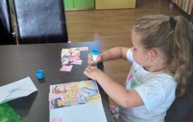 Dziewczynka przykleja na kartkę ułożone przez siebie puzzle z papieru z wizerunkiem księżniczek.