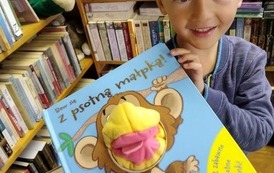 Chłopiec trzyma w ręku zabawkową książeczkę, uśmiecha się.