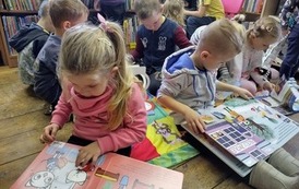 Dzieci siedzą na kocykach i przeglądają książeczki.