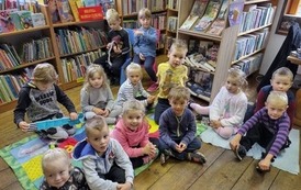 Grupa dzieci siedzących na kocykach w bibliotece.