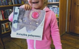 Dziewczynka w r&oacute;żowej bluzce pokazuje swoją nową książeczkę w bibliotece w Borzechowie.