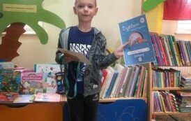 Chłopiec stoi w bibliotece w Pinczynie i pokazuje dypom Małego Czytelnika.