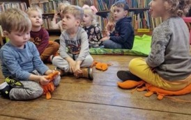 Dzieci siedzą na podłodze na poduszkach w bibliotece w Borzechowie