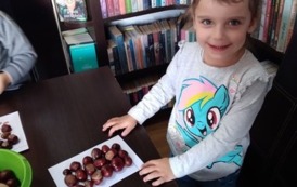 Dziewczynka stoi przy stoliku, na stole leży kartka obłożona kasztanami według wzoru.