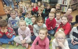 Grupa dzieci siedzi na dywanie i słucha bajki czytanej przez bibliotekarkę