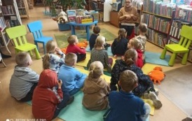Dzieci siedzą na karimatach i patrzą na Panią bibliotekarkę i słuchają co m&oacute;wi.