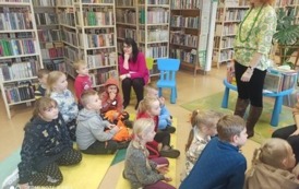 Dzieci siedzą na karimatach i słuchają bajkę czytaną przez bibliotekarkę. Widać też Panią nauczycielkę i Panią do pomocy.
