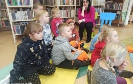 Dzieci siedza na karimatach i słuchają bajki. W tel widać Panią w r&oacute;żowej bluzce siedzącą na krzesełku.