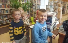 Na przedzie dwoje chłopc&oacute;w czekających w kolejce przy biurku, za nimi stoją dwie dziewczynki