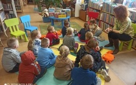 Dzieci siedzą na karimatach. Na krzesełku siedzi przy nich Pani nauczycielka