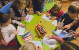 Dzieci siedzą przy okrągłym zielonym stoliku i robią pracę plastyczną.