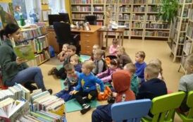 Dzieci siedzą na karimatach w bibliotece w Zblewie,a bibliotekarka czyta bajkę.