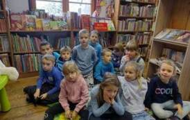 Dzieci siedzą na dywanie i słuchają bibliotekarki.