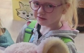 Dziewczynka o blond włosach w okularach trzyma dużego misia.
