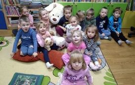 Dzieci siedzą w grupie na dywanie z białym dużym miesiem po środku.