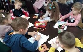 Dzieci siedzą przy stole i kolorują misie.