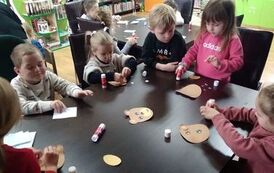 Dzieci siedzą przy stole i wyklejają papierowego misia