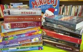 Nowe książki leżą na stoliku ułożone poziomo w bibliotece w Borzechowie. Jedna książka o Mikołaju ułożona z tyłu pionowo.