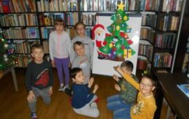 Dzieci stoją przy tablicy na kt&oacute;rej jest przyklejona, przystrojona choinka filcowa z Mikołajem.