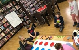 Pięcioro dzieci gra w grę rozłożoną na dywanie o nazwie TWISTER