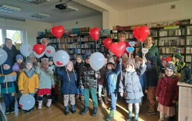 Grupa dzieci wraz z nauczycielami i bibliotekarką stoją trzymając baloniki walentynkowe