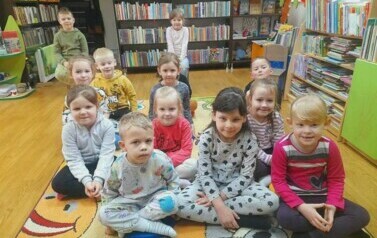Dzieci siedzą na dywanie i słuchają bajki czytanej przez bibliotekarkę.