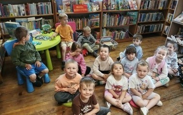 Dzieci siedzą na siedziskach i przy stoliczku i słuchają bajki