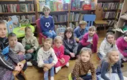 Dzieci siedzą w bibliotece w Borzechowie na siedziskach i krzesłach biorąc udział w zajęciach
