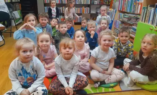 Dzieci siedzą na dywanie i siedziskach i słuchają bajki.