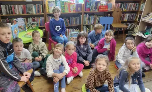 Dzieci siedzą w bibliotece w Borzechowie na siedziskach i krzesłach biorąc udział w zajęciach