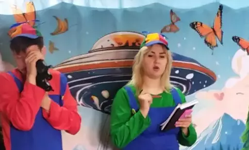 Mężczyzna i kobieta ubrani w niebieskie kombinezony. Mężczyzna trzyma lornetkę, a kobieta notes i długopis. W tle statek kosmiczny i motyle na niebie.