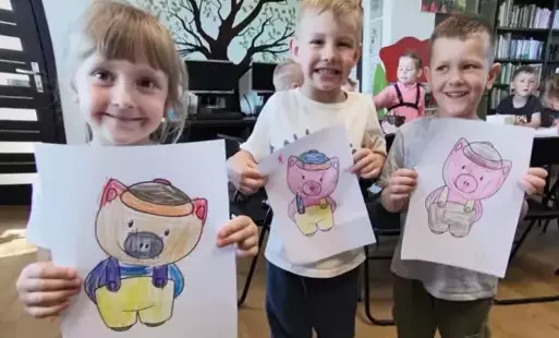 Dziewczynka i dwóch chłopców pokazują na kartkach swoje pokolorowane świnki.