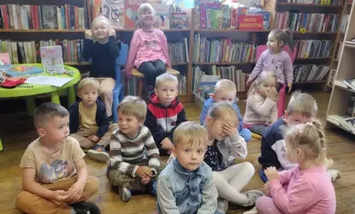 Dzieci siedzą na siedziskach i krzesełkach i słuchają bajki.