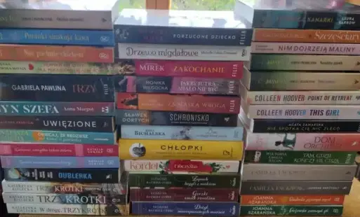 Na stole leżą pionowo trzy rzędy nowych książek z widocznymi tytułami.
