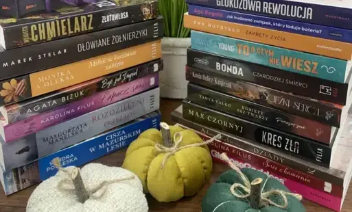 Na stole leżą książki ułożone pionowo, przy nich leżą dynie dekoracyjne