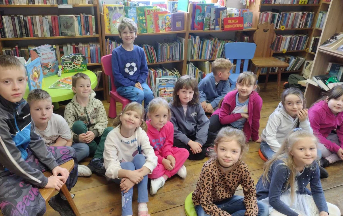 Dzieci siedzą w bibliotece w Borzechowie na siedziskach i krzesłach biorąc udział w zajęciach