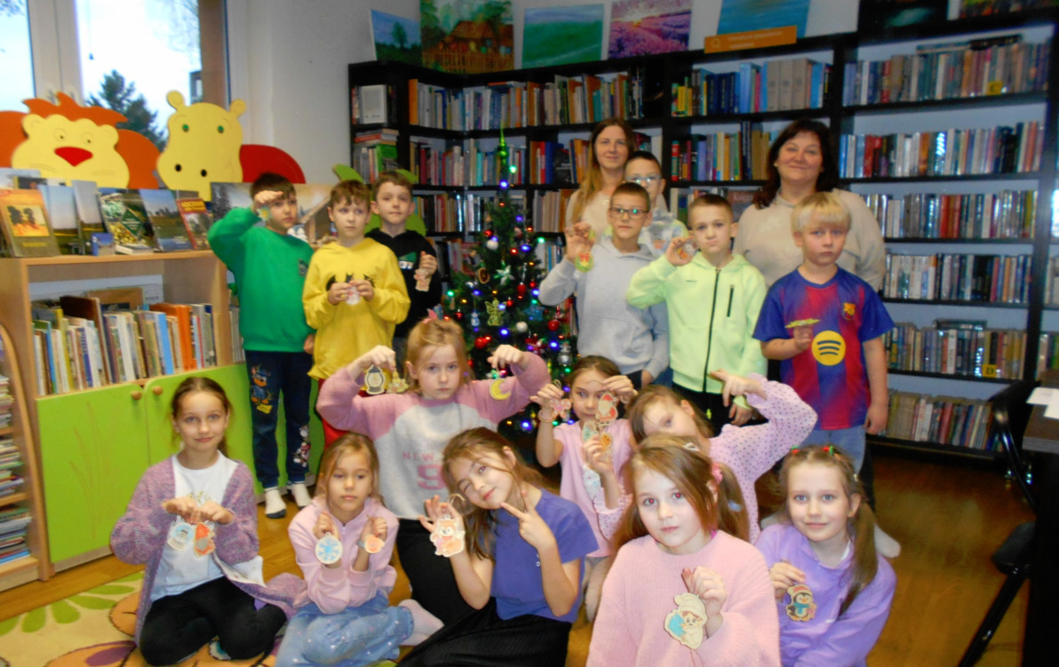 Grupa dzieci stoi ze swoimi Paniami przy choince i trzyma przyozdobione przez siebie drewniane bombki.